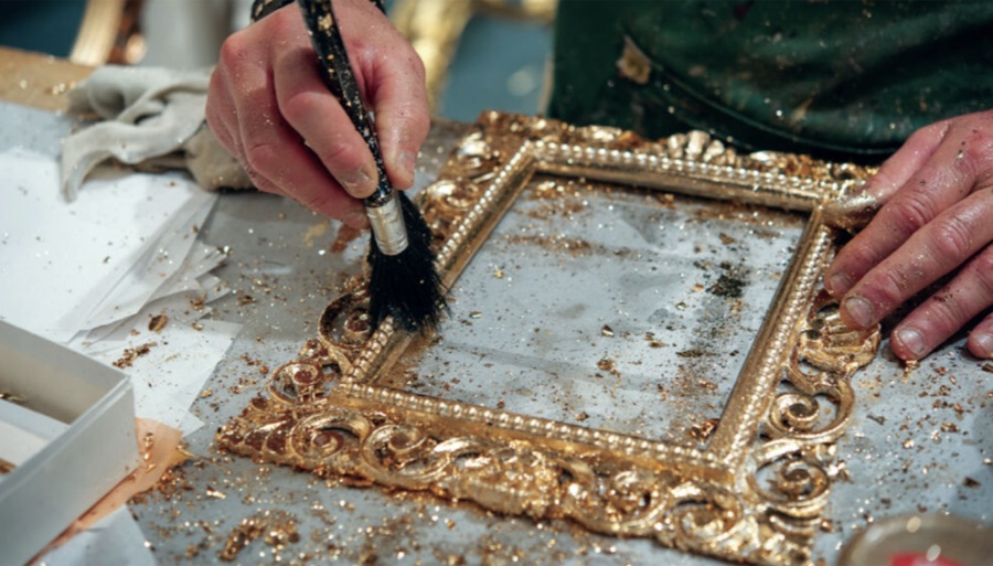 Craftsman applying gold leaf to a Louis frame by hand